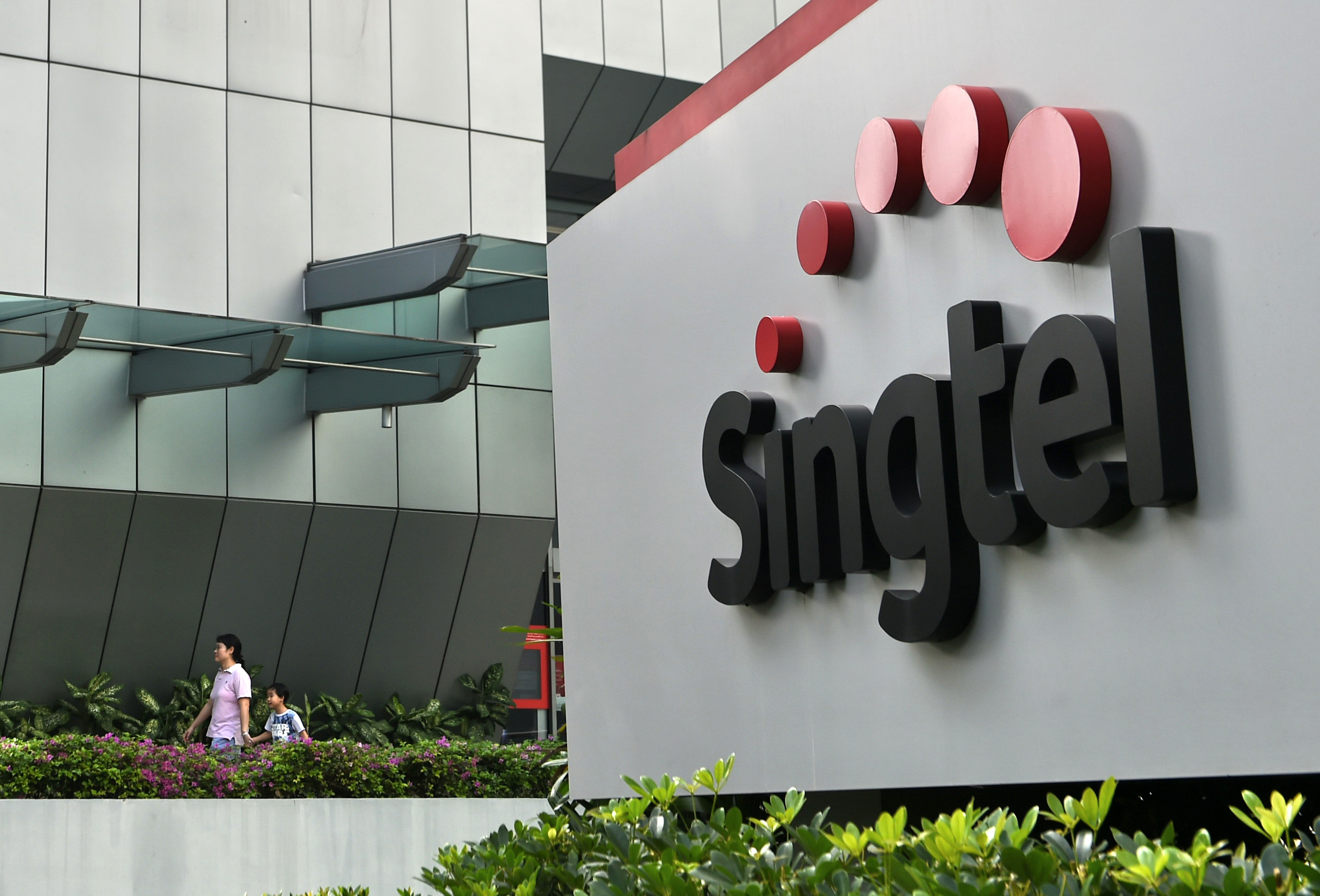 A woman and a child walk out of the Singapore Telecommunications (Singtel) building in Singapore on February 12, 2016.  Singtel reported a 1.7 per cent fall in third-quarter net profit of 683 million US dollar for the three months ended December, compared with 694 million US dollar a year ago, as adverse currency movements and investments offset growing mobile data usage by its customers.  AFP PHOTO / ROSLAN RAHMAN / AFP PHOTO / ROSLAN RAHMAN