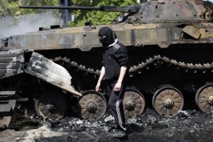 A masked man walks past a burnt-out armoured personal carrier near the city hall in Mariupol, eastern Ukraine May 10, 2014. CREDIT: REUTERS/MARKO DJURICA