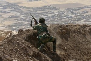 A Kurdish Peshmerga fighter moves into position while firing into Baretle village, which is controlled by the Islamic State, in Khazir