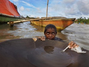 Jonathon Ramorez, 12, stands waist-deep in the bay with a wooden pan he uses to separate gold from sediment. He will spend hours in the water, which often is tainted with animal waste and teeming with bacteria. Image by Larry C. Price. Philippines, 2013. 