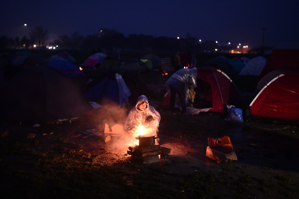 A man tries to cook on an open fire under the rain at a makeshift camp at the Greek-Macedonian border near the village of Idomeni, where thousands of refugees and migrants are stranded on March 7, 2016.  EU leaders held a summit with Turkey's prime minister on March 7 in order to back closing the Balkans migrant route and urge Ankara to accept deportations of large numbers of economic migrants from overstretched Greece. / AFP / LOUISA GOULIAMAKI