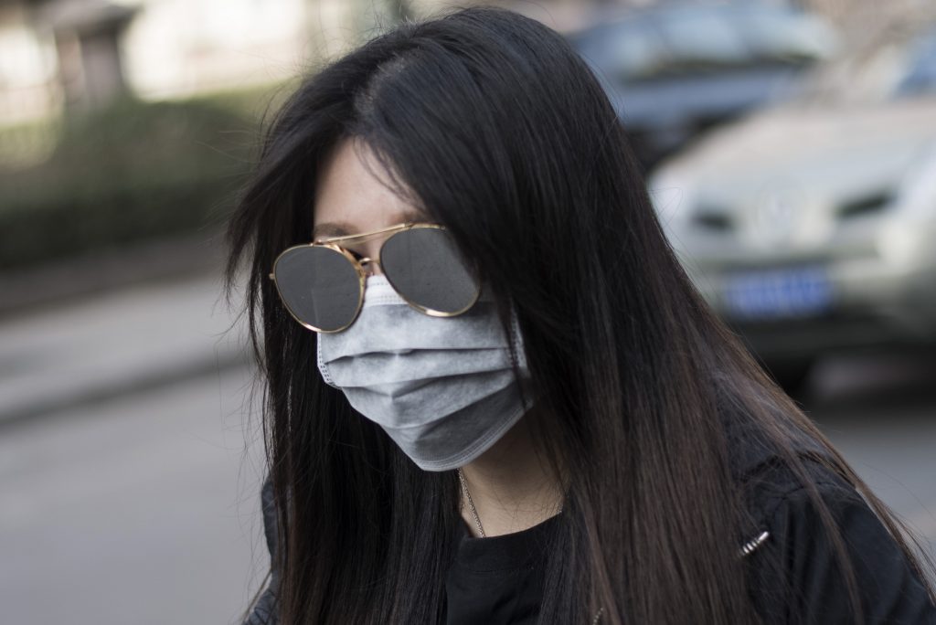 A woman wears a face mask while crossing a road during a yellow alert for air pollution in Beijing on March 18, 2016. / AFP PHOTO / FRED DUFOUR