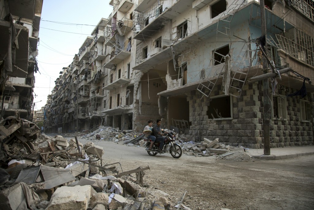 Syrian men ride a motorbike past damaged buildings in the rebel-held Bustan al-Qasr district in eastern Aleppo, on May 4, 2016. The Syrian army said late on May 4 that it had agreed to calls from Russia and the United States for a two-day truce in Aleppo that would begin from 1:00 am on May 5.  Renewed fighting in recent days, especially in and around Aleppo, had threatened the full collapse of the February 27 ceasefire agreement, a landmark in attempts to finally resolve a conflict that has left more than 270,000 dead. / AFP PHOTO / KARAM AL-MASRI