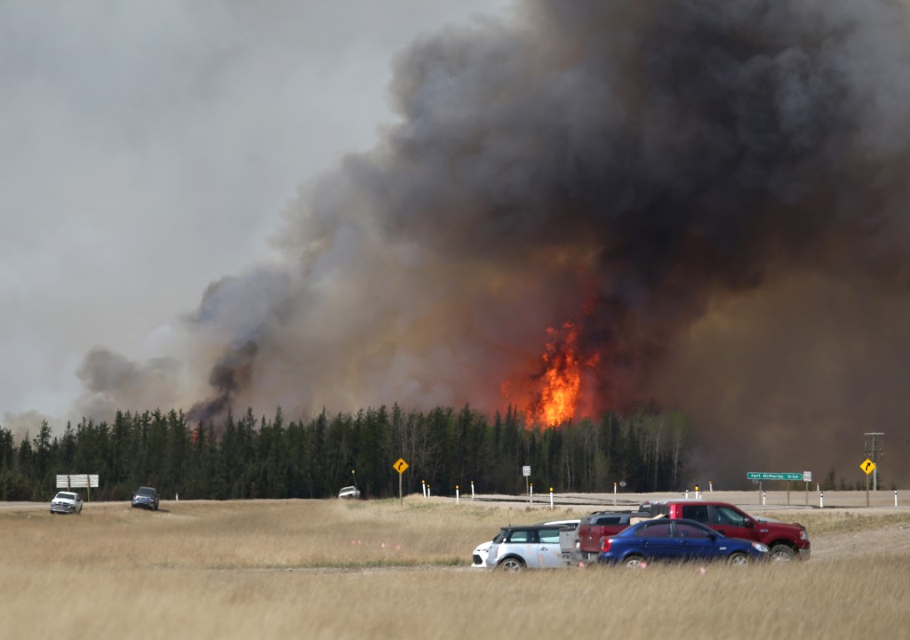 A convoy of evacuees drives south as flames and smoke rises along the highway near near Fort McMurray, Alberta on May 6, 2016. Canadian police led convoys of cars through the burning ghost town of Fort McMurray Friday in a risky operation to get people to safety far to the south.In the latest chapter of the drama triggered by monster fires in Alberta's oil sands region, the convoys of 50 cars at a time are driving through the city at about 50-60 kilometers per hour (30-40 miles per hour) TV footage showed. / AFP PHOTO / Cole Burston/