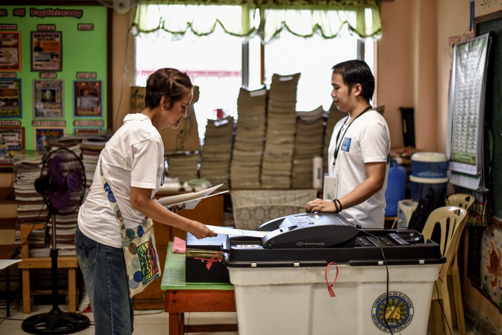 An elderly Filipino woman (L) places her ballot paper into a vote counting machine during the presidential and vice presidential elections at a polling center in Manila on May 9, 2016. Voting was underway in the Philippines on May 9 to elect a new president, with anti-establishment firebrand Rodrigo Duterte the shock favourite after an incendiary campaign in which he vowed to butcher criminals. / AFP PHOTO / MOHD RASFAN