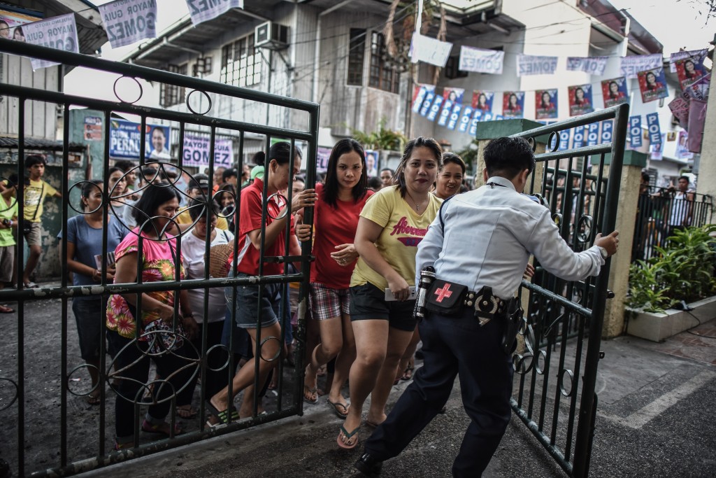 A security guard (R) opens the gate for voters to enter during the presidential and vice presidential elections at a polling center in Manila on May 9, 2016.  Voting was underway in the Philippines on May 9 to elect a new president, with anti-establishment firebrand Rodrigo Duterte the shock favourite after an incendiary campaign in which he vowed to butcher criminals. / AFP PHOTO / MOHD RASFAN