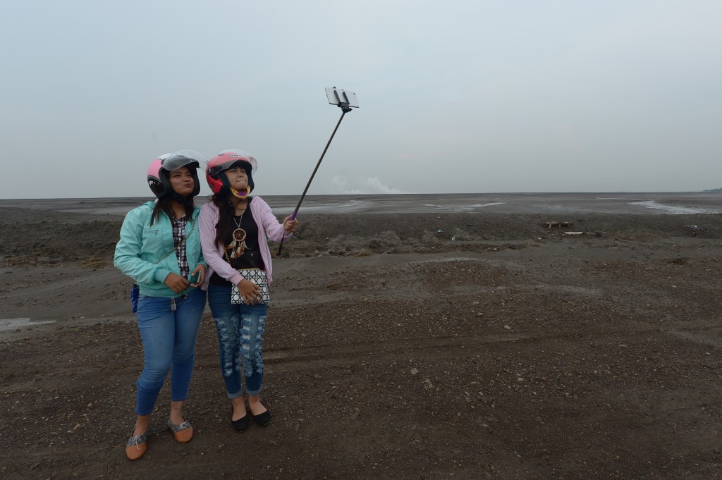 This picture taken on March 28, 2016 shows Indonesian tourists taking selfies at a mud volcano area in Sidoarjo, East Java.  A mud volcano that erupted in central Indonesia a decade ago and swallowed entire villages is still oozing its all-consuming sludge, but for some entrepreneurial locals it has provided an unlikely business opportunity. "Mud tourism" is booming, as visitors flock to see rooftops poking above the giant bubbling lake, life-size statues made of mud and haunting memorials to one of the countrys worst environmental disasters.  / AFP PHOTO / ADEK BERRY / To go with AFP story 'Indonesia-science-mud-volcano-tourism',FEATURE by Nick Perry