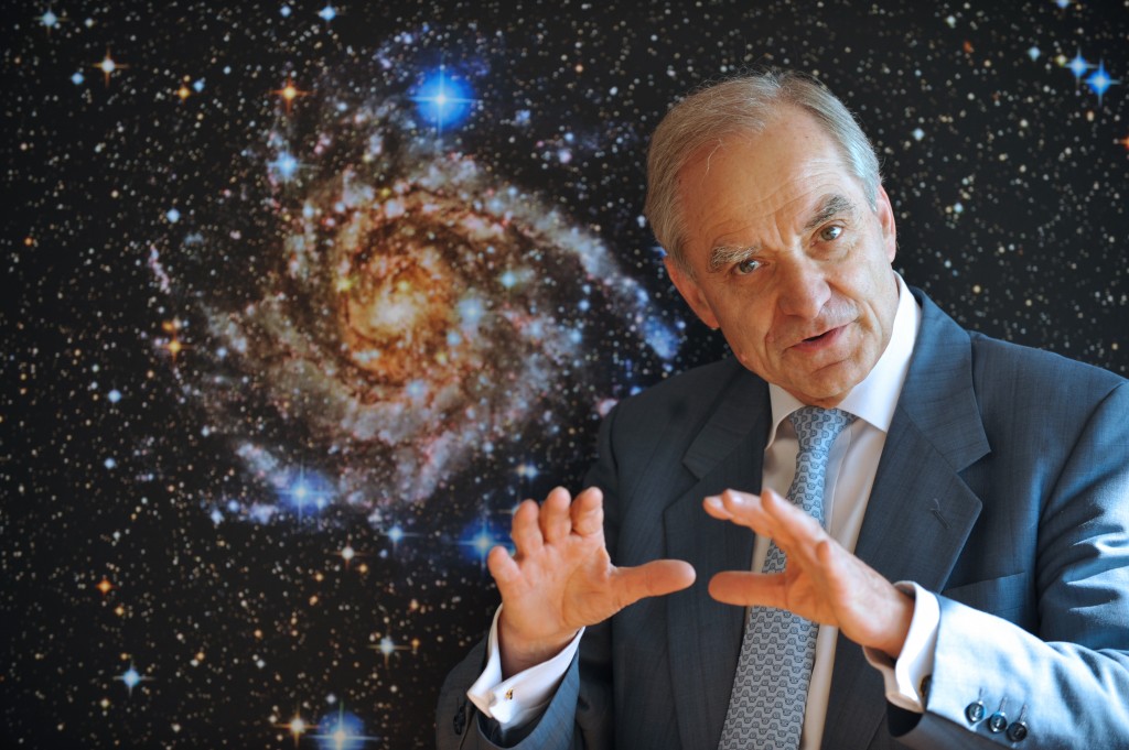 French astrophysician Andre Brahic poses in front of a picture of the IC 342 galaxy on May 19, 2009 at the headquarters of the French Atomic energy commission Saclay. AFP PHOTO ERIC FEFERBERG / AFP PHOTO / ERIC FEFERBERG