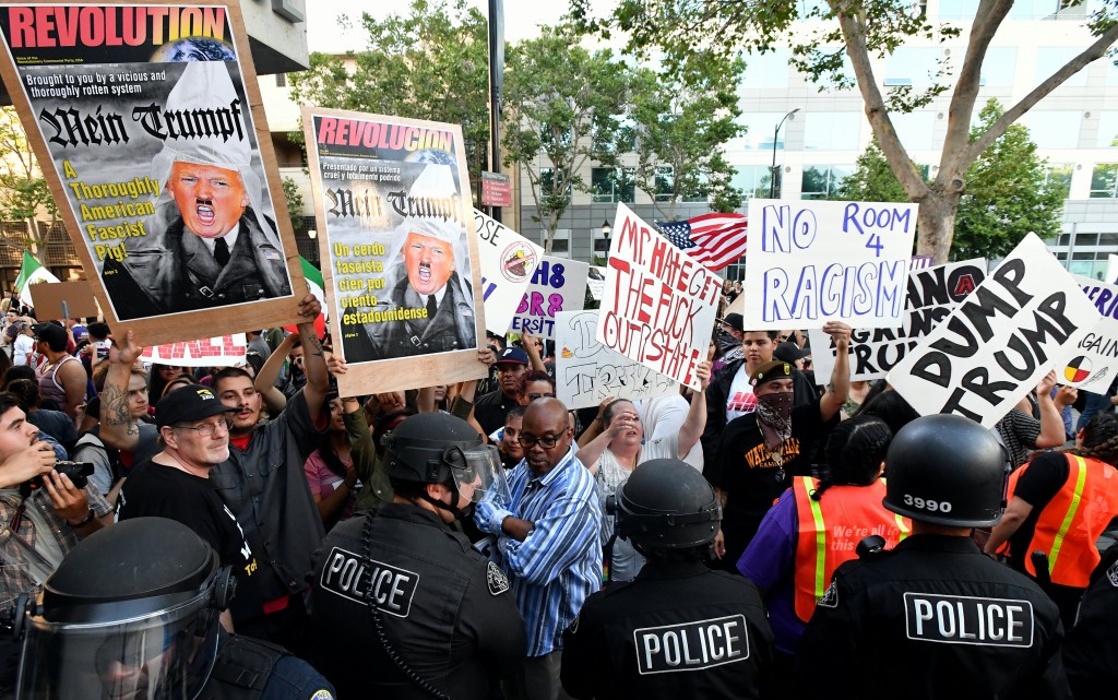 Protesters hold up signs against a police skirmish line near where Republican presidential candidate Donald Trump holds a rally in San Jose, California on June 02, 2016.  Protesters attacked Trump supporters as they left the rally, burned an american flag, trump paraphernalia and scuffled with police and each other. / AFP PHOTO / JOSH EDELSON