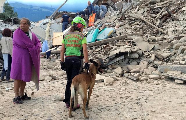 A man wrapped in a blanket looks on as a rescuer with a dog stand in front a collapsed house following a quake in Amatrice, central Italy, August 24, 2016. REUTERS/Emiliano Grillotti