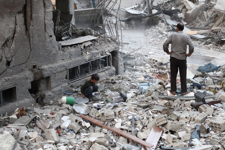 A Syrian boy collects items amidst the rubble of destroyed buildings on October 3, 2016, following reported air strikes in the rebel-held town of Douma, on the eastern outskirts of the capital Damascus. Air strikes shook a besieged rebel-held town east of the Syrian capital, sparking fears among civilians of a fate similar to battered Aleppo city. More than a dozen raids and several mortar rounds pounded Douma, said the Syrian Observatory for Human Rights monitoring group.  / AFP PHOTO / Abd Doumany