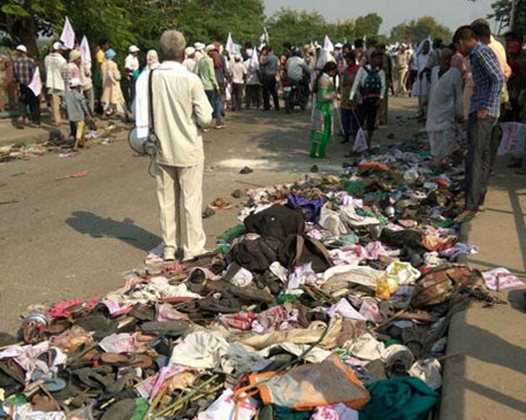 Indian bystanders gather near discarded belongings at the roadside following a fatal stampede in Varanasi on October 15, 2016. A stampede at a religious gathering in northern India killed at least 19 people October 15 as thousands of devotees of a controversial guru tried to cross a bridge at once, police said. The followers of Jai Gurudev, a leader of a local religious sect, had gathered on the outskirts of Varanasi, a Hindu holy town on the banks of river Ganges in Uttar Pradesh state, when the deadly stampede broke out. / AFP PHOTO / STR