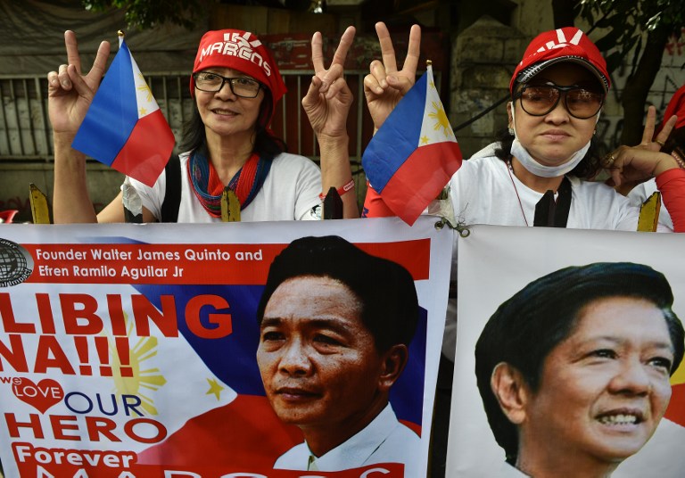 Supporters of the late dictator Ferdinand Marcos flash the "V" sign behind portraits of Marcos (L) and his son, former senator Bongbong Marcos, at the start of a vigil in front of the Supreme Court in Manila on October 17, 2016. Imee Marcos, daughter of the late dictator Ferdinand Marcos, called for forgiveness on October 17 as she led a rally at the Supreme Court urging it to approve a controversial hero's burial for her father. / AFP PHOTO / TED ALJIBE