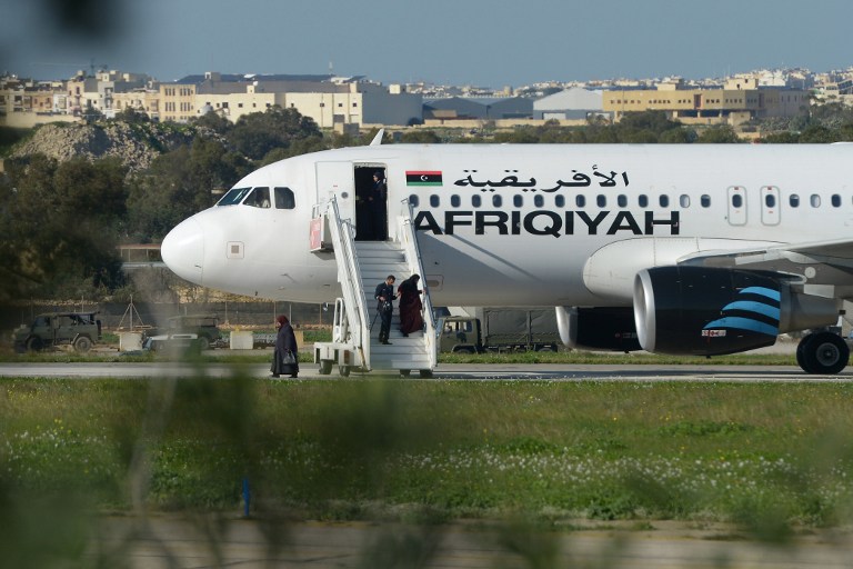 A picture taken on December 23, 2016 in Valletta, Malta, shows a crew member helping a group of hostages to disembark from the Afriqiyah Airways A320 after it was hijacked from Libya. A man who said he was armed with a grenade hijacked a Libyan plane which landed on Malta Friday with 118 people on board, Malta's prime minister and government sources on the Mediterranean island said. After more than an hour on the tarmac, the plane's door opened and a first group of women and children were seen descending a mobile staircase. "First group of passengers, consisting of women and children, being released now," Prime Minister Joseph Muscat said on Twitter, adding in a later tweet that 50 passengers in all were being let off the plane. / AFP PHOTO / Matthew Mirabelli / Malta OUT