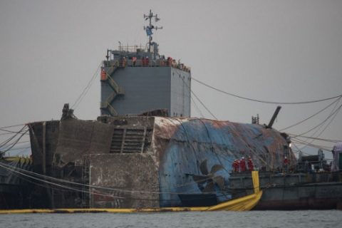 Workers stand before a propellor of the wreck of the Sewol ferry during its the salvage operation off the coast of South Korea's southern island of Jindo on March 24, 2017. South Koreas sunken Sewol ferry emerged from the waters March 23, nearly three years after it went down with the loss of more than 300 lives and dealt a crushing blow to now-ousted president Park Geun-Hye. / AFP PHOTO / AFP PHOTO AND POOL / Ed JONES