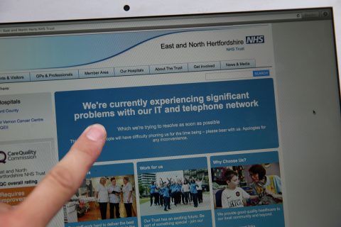 In this posed picture photograph, a woman points to the website of the NHS: East and North Hertfordshire notifying users of a problem in its network, in London on May 12, 2017. Several British hospitals were hit by cyber attacks on Friday, the country's health service said, forcing some to divert ambulances to other clinics and urge people not to try to contact their doctors. / AFP PHOTO / Daniel LEAL-OLIVAS